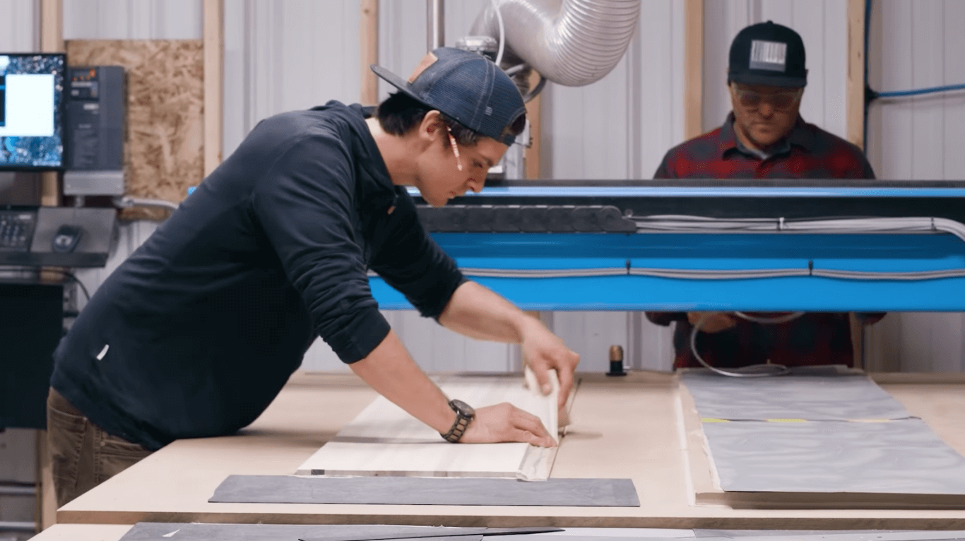 a student taping down a board on a cnc bed